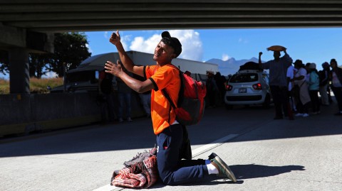 A Central American man traveling with a migrant caravan heading for the US border kneels to beg for a ride on the highway connecting Guadalajara with Tepic, Mexico, on Nov. 13, 2018. Photo: Rodingo Abd / AP