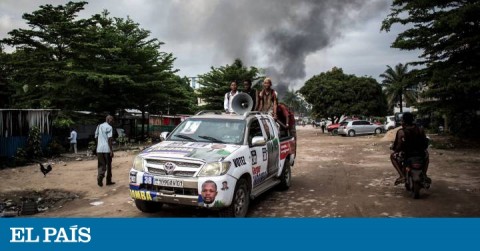 Un automóvil con propaganda electoral cerca de un incendio en un almacén de máquinas para votar, este jueves en Kinshasa