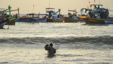 A fisherman walks into the water in front of boats in Vietnam