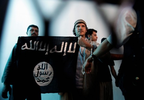 In this April 23, 2013, photo a suspected Yemeni al-Qaida militant, center, holds a banner as he stands behind bars during a court hearing in state security court in Sanaa, Yemen. (AP Photo/Hani Mohammed)